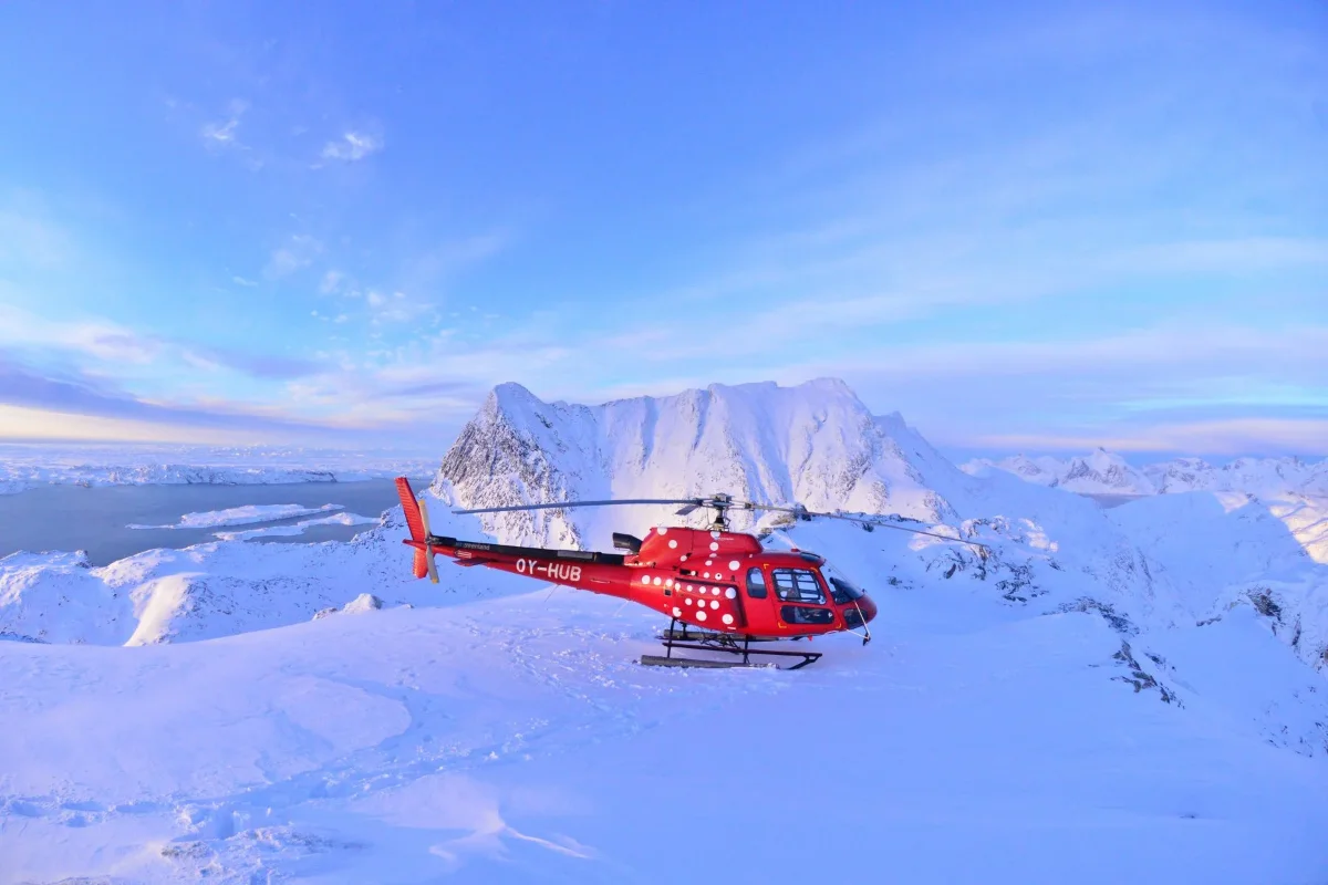 A red helicopter is parked on a snowy mountain ridge.