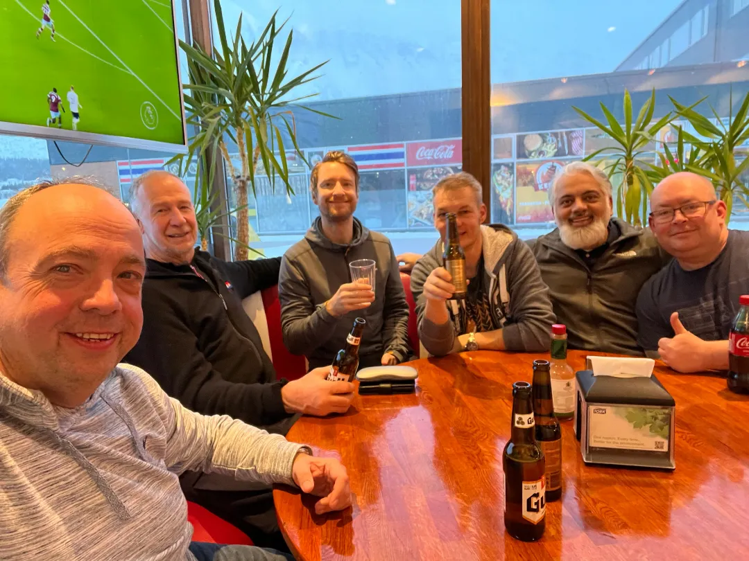 Tour guides David Gibbon and Conrad Dickinson sitting with four clients around a table in a restaurant, holding drinks and smiling at the camera.