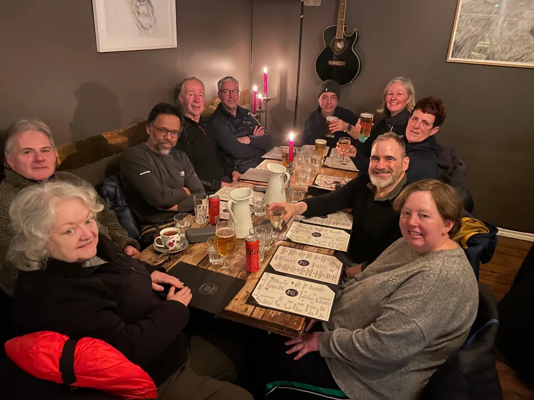 Tour guides David Gibbon and Conrad Dickinson with a group of clients sitting around a table in a restaurant. Some are holding drinks and laughing.