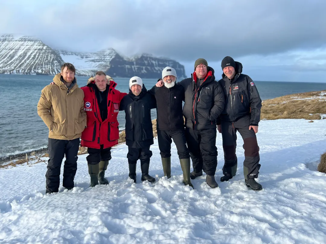 Tour guides David Gibbon and Conrad Dickinson with four clients in winter jackets all standing together and smiling in a snowy landscape by the sea.