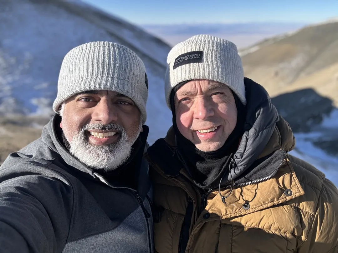 A client with a white-flecked beard smiles for a selfie with tour leader David Gibbon on a snow-covered mountain.